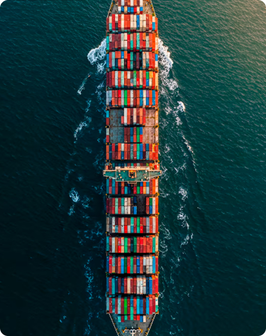 Aerial view of a large cargo ship carrying colorful shipping containers moving through dark blue ocean water.