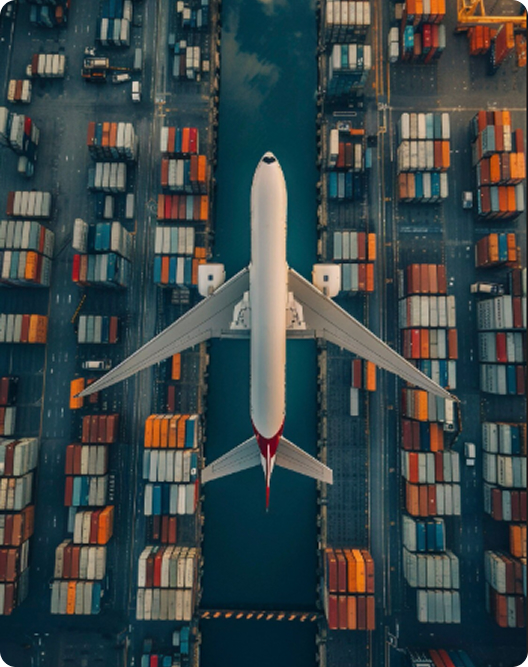 Aerial view of a white airplane flying over a cargo port with rows of colorful shipping containers on both sides.